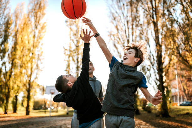 Two boys playing basketball with dad on sport field during weekend, outdoor
