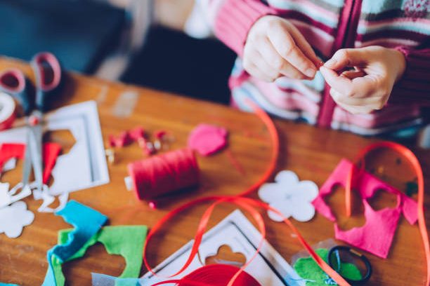 tailor art workshops for children - a girl sewing felt decorations - colorful fabrics lying on a table