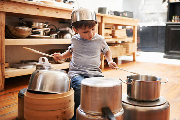A young boy playing drums on pots and pans