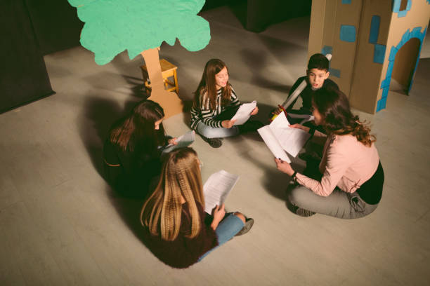 Group of children enjoying drama club rehearsal. They are sitting and reading script with their drama teacher.